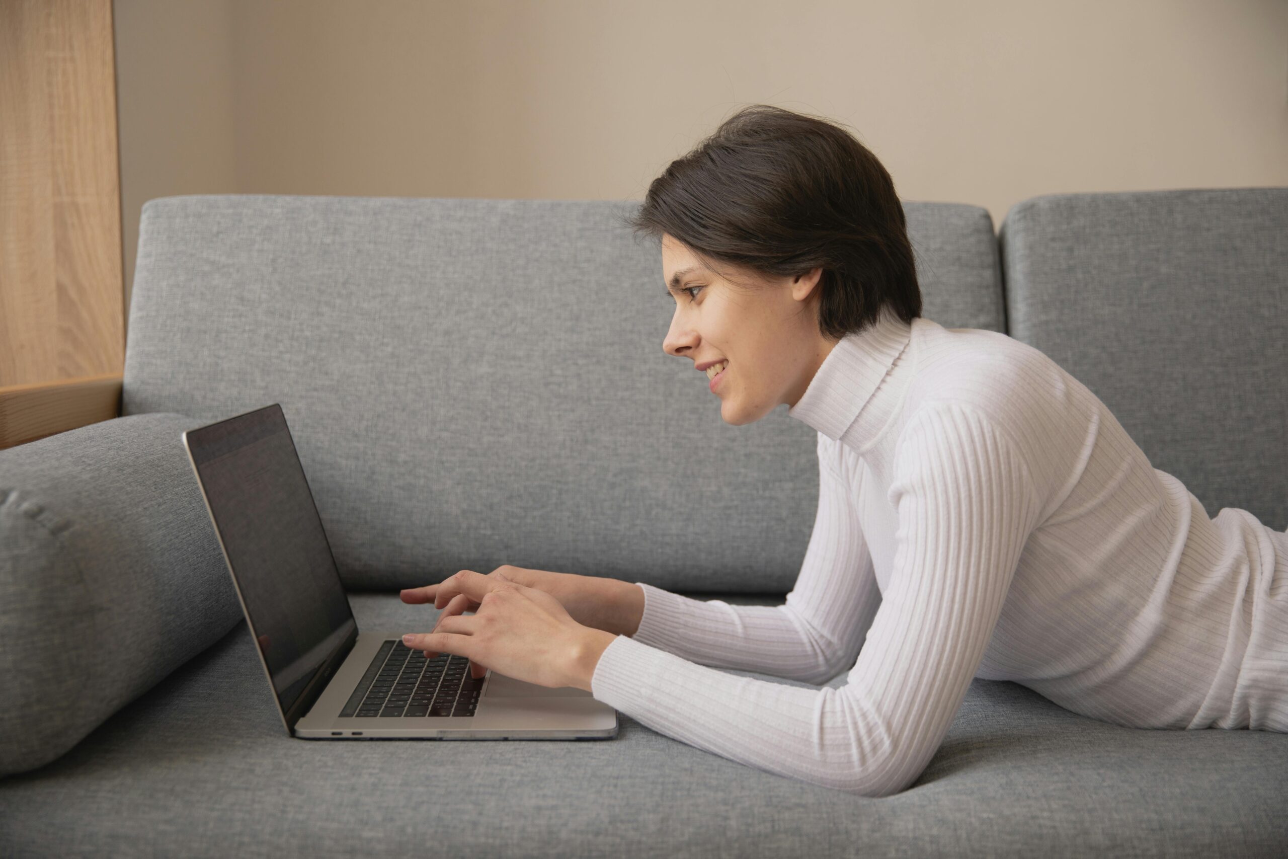 Online Classes Woman working remotely on a laptop at home, lying on a comfortable sofa.