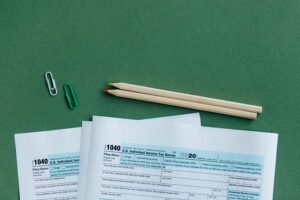 U.S. tax forms with pencils and paperclips on green surface in a flat lay setup.